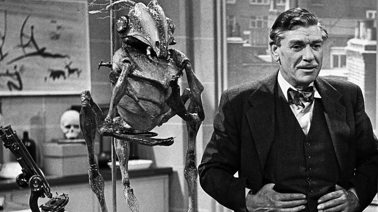 Black and white image of a man in a suit with his back to an insectoid alien