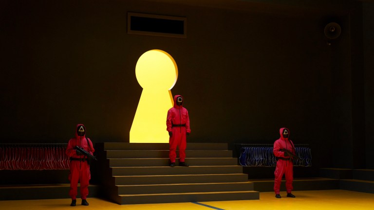 Squid Game guards stand in front of a lit up keyhole in Squid Game season 3