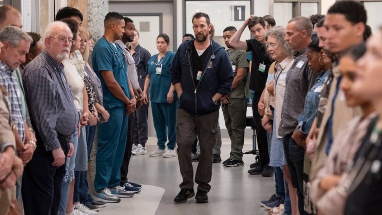 Noah Wylie stands in a hospital hallway in Max medical drama The Pitt.